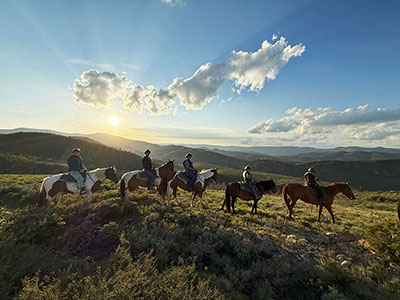 Five horseback riders pause for a picture with a westering sun in the background.