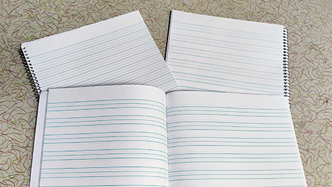 Student notebooks displayed showing samples of cursive and manuscript line styles and spiral vs. stapled bindings.